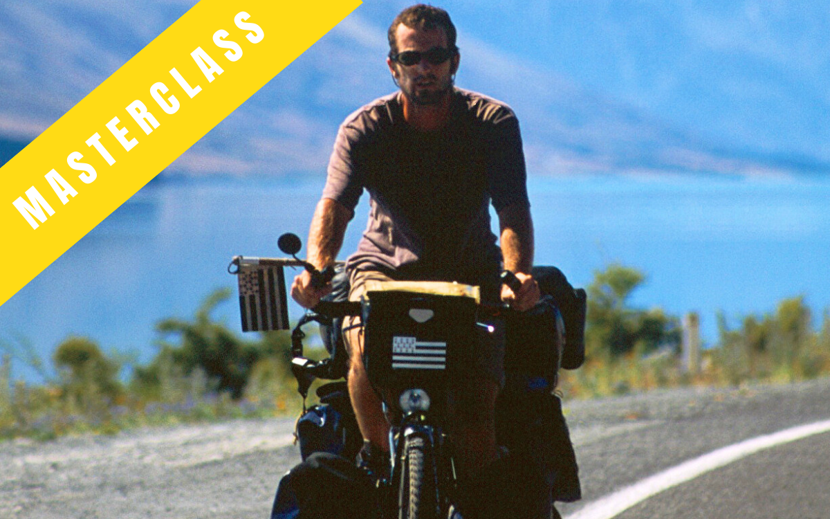 masterclass vélo brieg jaffrès sur son vélo rempli de sacoches, arrière plan montagne