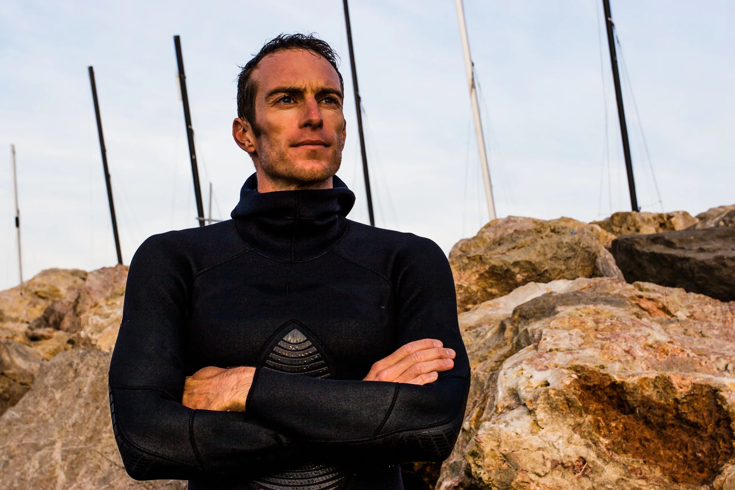 Portrait de Morgan Bourd'his, bras croisés, en tenue de plongée, fond de rochers et de mâts de bateau. Peut-être chez lui à Marseille