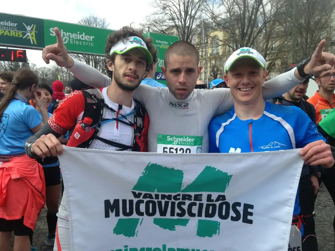 Paul avec deux comparses qui tendent le drapeau "vaincre la mucoviscidose".