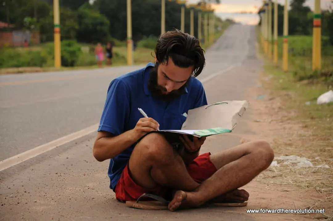Benjamin Lesage assis au bord de la route, carnet en main, écrit.