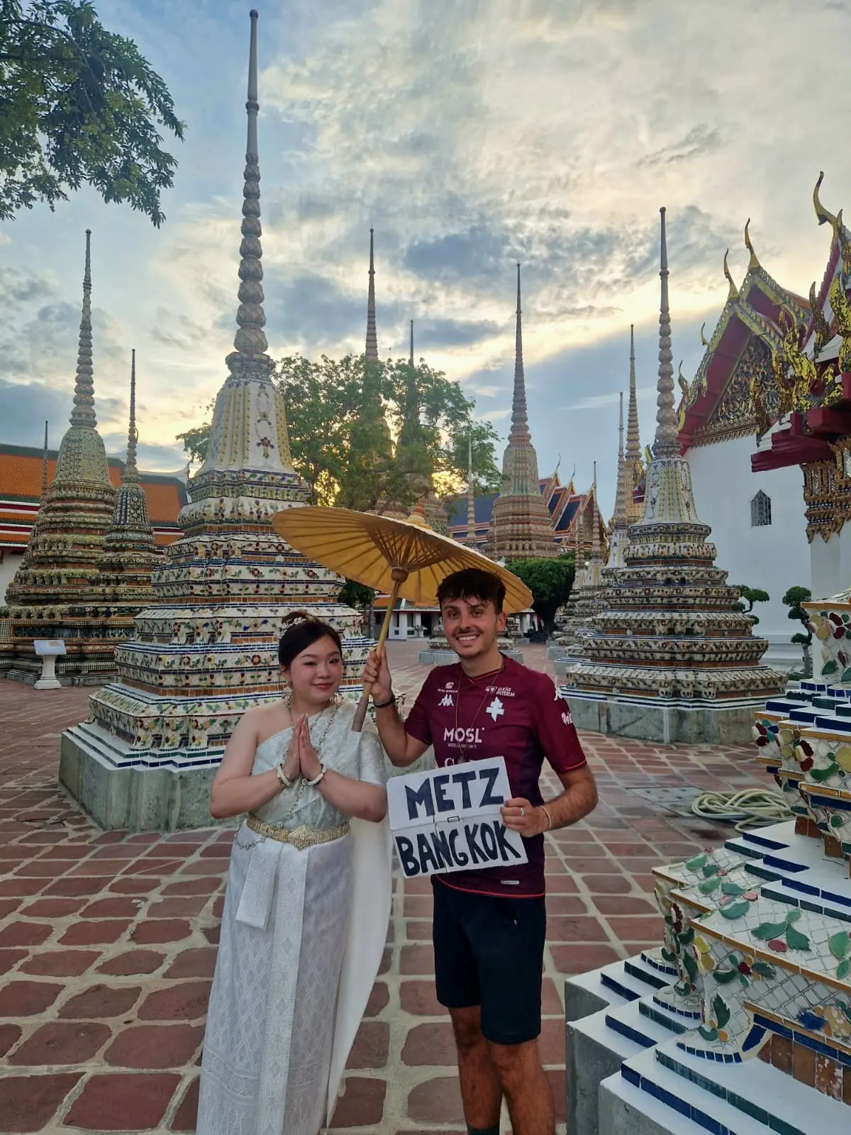jules riss en thailande devant un temple en compagnie d'une thailandaise en constume traditionnel... avec sa pancarte d'autostoppeur bien sûr